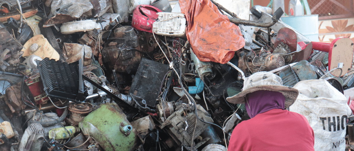 a worker sitting in front of a large pile of plastic e-waste