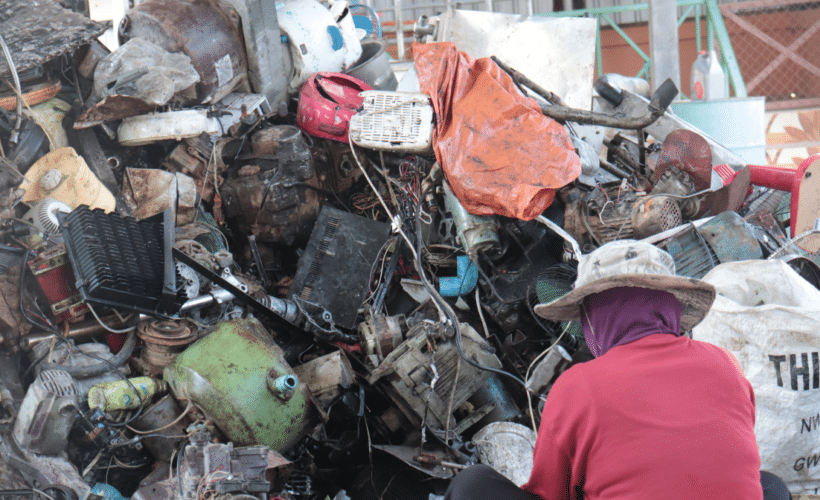 a worker sitting in front of a large pile of plastic e-waste
