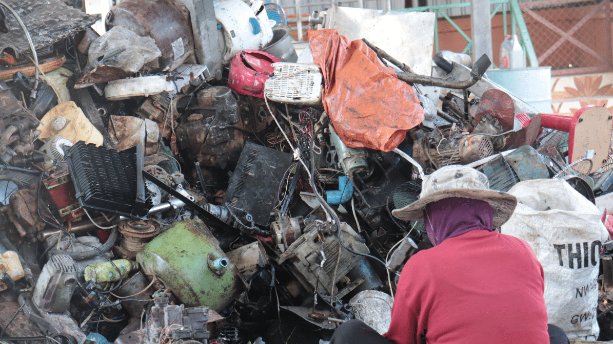 a worker sitting in front of a large pile of plastic e-waste
