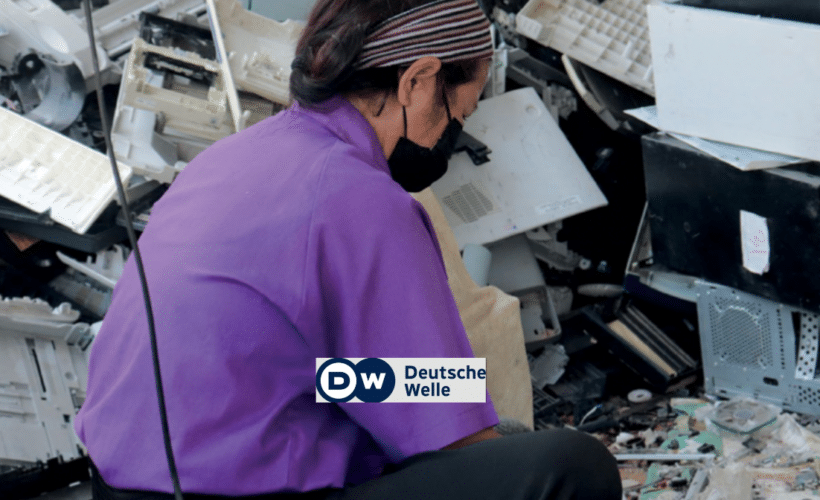 a woman recycling worker sitting in a pile of plastic e-waste, DW logo in foreground