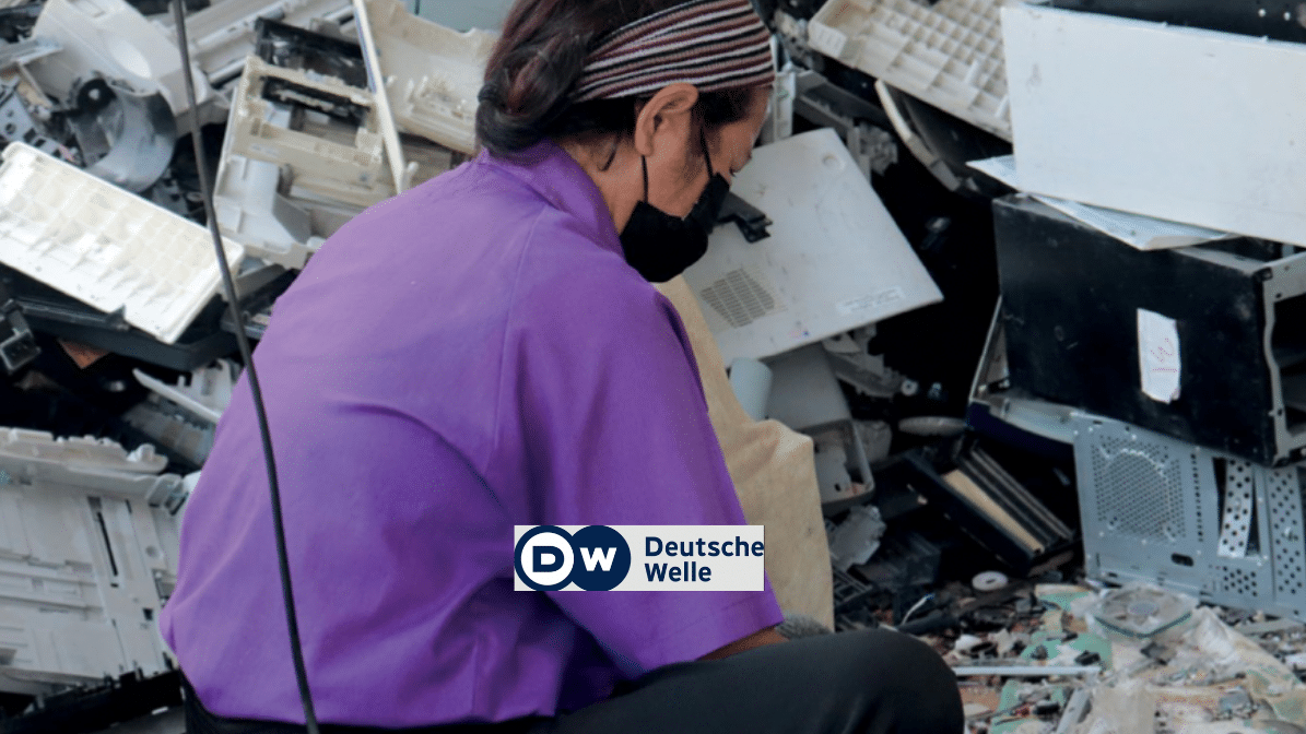 a woman recycling worker sitting in a pile of plastic e-waste, DW logo in foreground