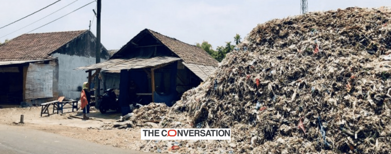 a huge pile of plastic waste next to a house, logo of The Conversation in foreground