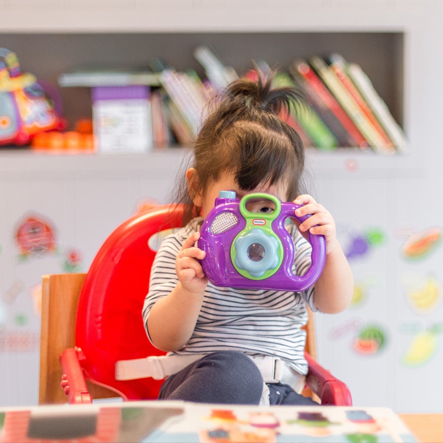 a young girl in a high chair holding a plastic toy in front of her face